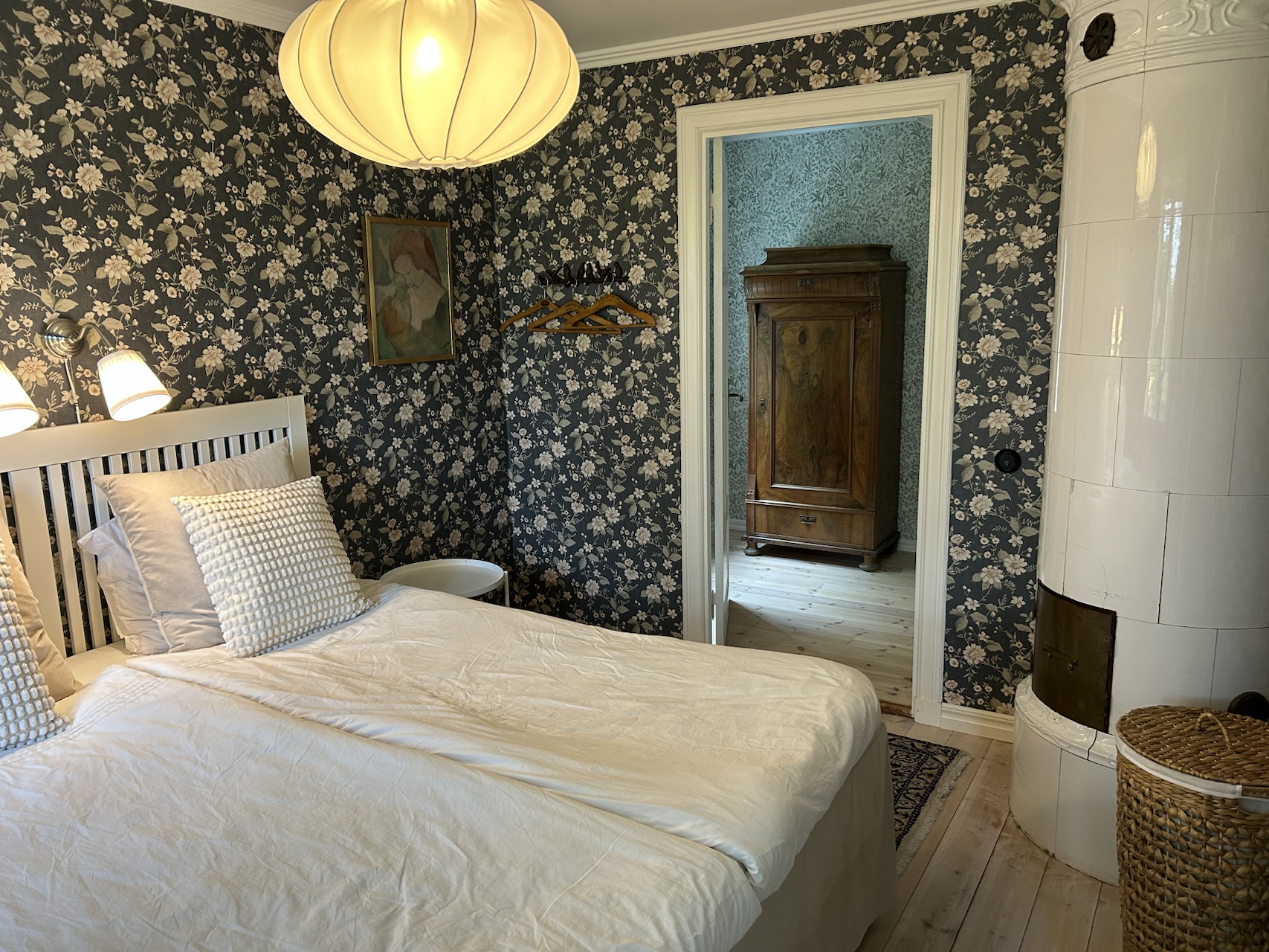 Second view of bedroom one showing the bed, patterned wallpaper and antique wardrobe