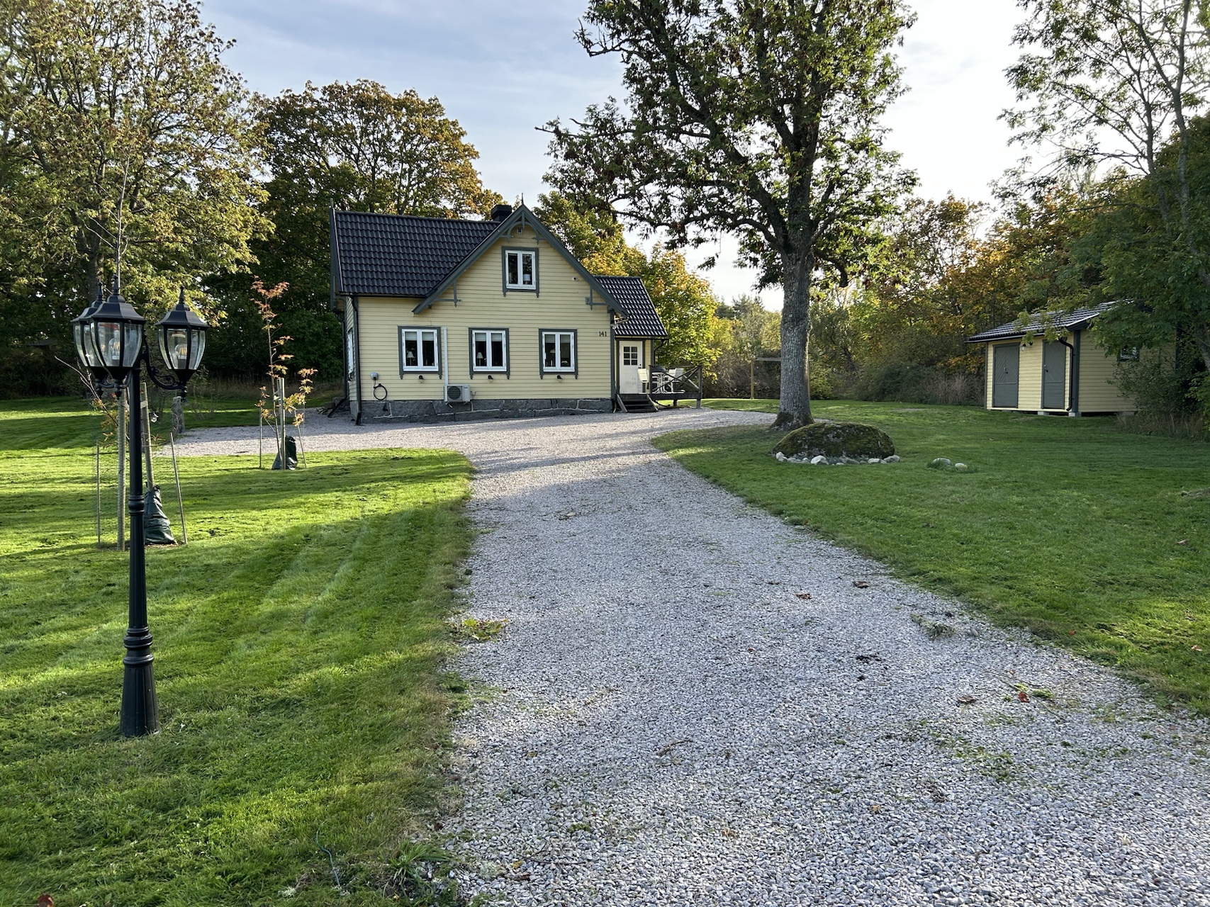 Villa Millegarne viewed across the gravel drive, with mature trees and the garden outbuilding