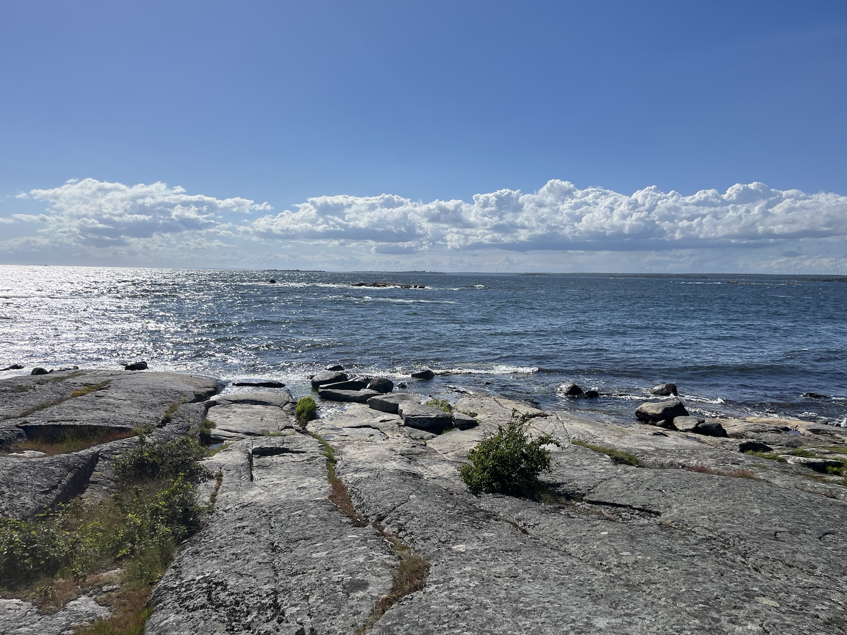 Rocky shoreline and calm sea beneath a bright, cloud-dotted sky